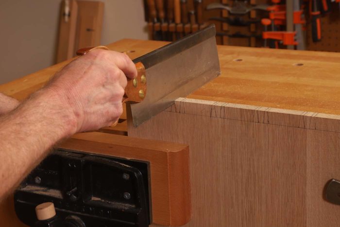 With the dovetails laid out and the tail board mounted at the edge of my bench in the shoulder vise, I define the tails with sawcuts.