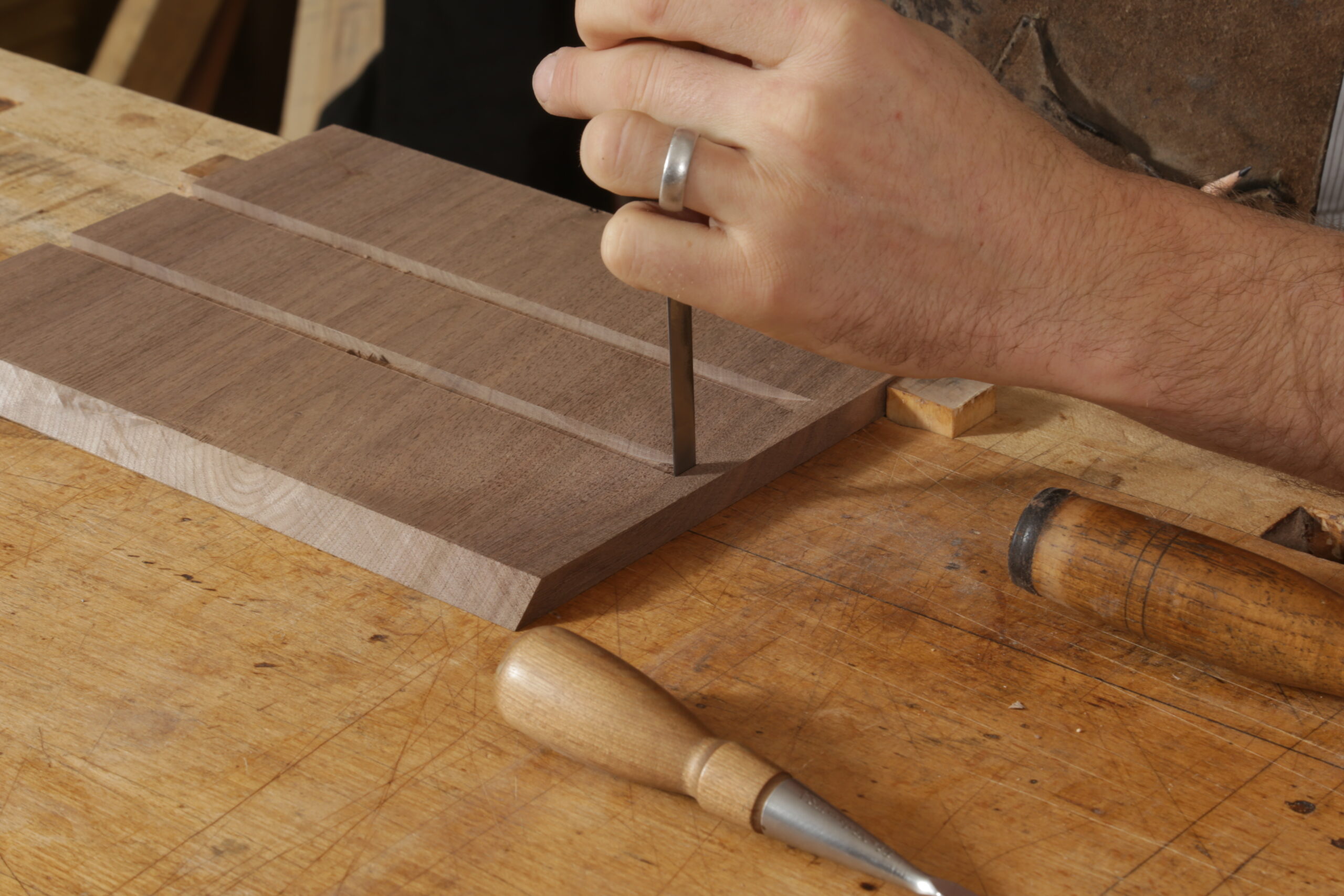 The author using a chisel to square up a dado. He is holding one chisel in his hand, and the handles of two others are in shot. There are two dadoes on the inside of the box side.