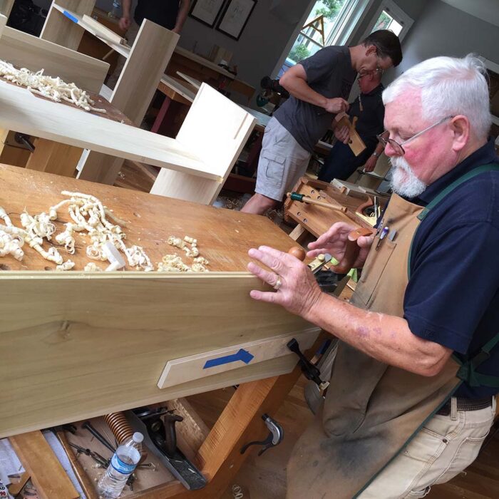 A man using a grooving plane to create a tongue and groove joint on a piece of poplar