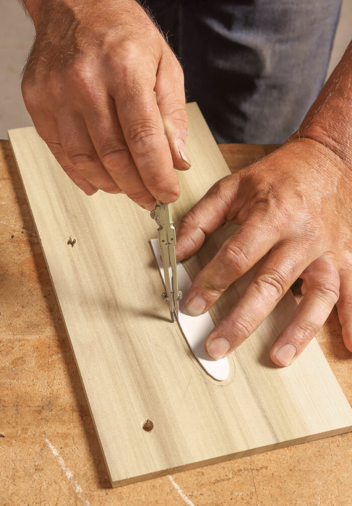 Small scale scribing. Lay the paper feather template on the blank for the router template, and scribe around the feather with the compass set to the dimension of the bit to the bushing.