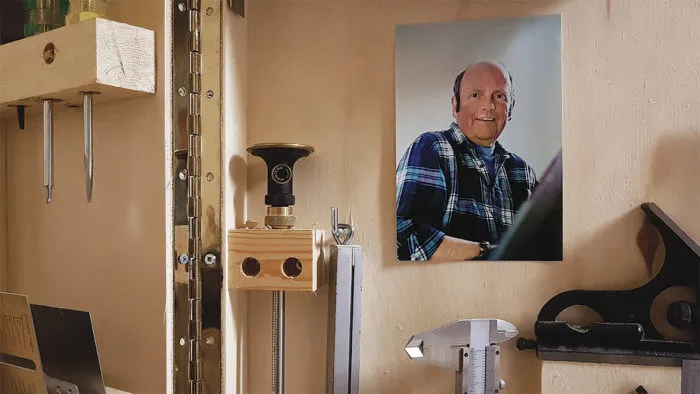 A selection of woodworking hand tools are hung on a wall with a picture of a man wearing a plaid shirt. 