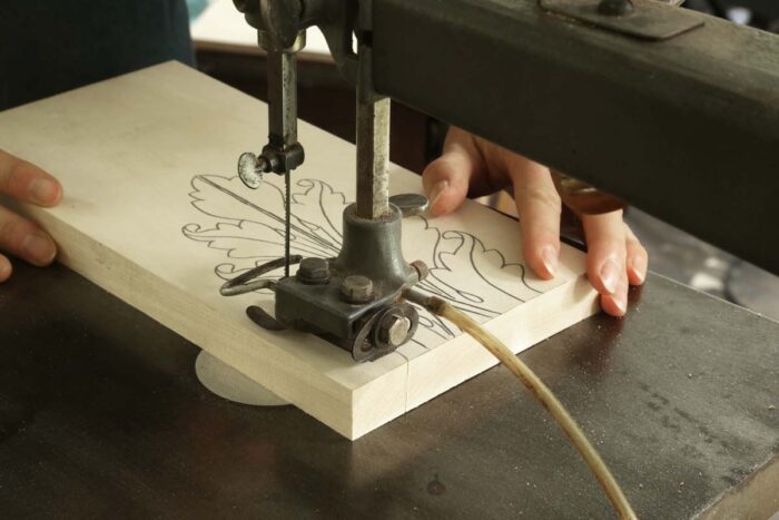 Mary cuts out the parameter of the leaf at the scroll saw.