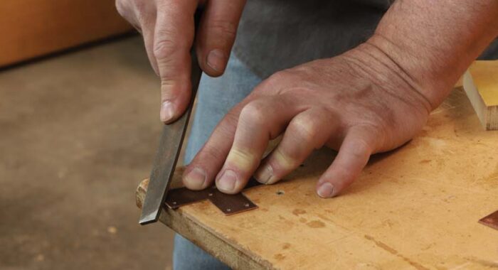 The corner of a piece is being filed at the edge of a workbench