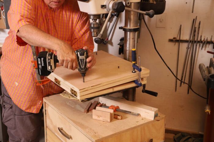 Beth screws a sacrificial sheet of plywood to the angled drill press jig. 