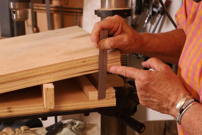 Beth uses a ruler to measure the gap in the angled drill press jig so she can cut an accurately sized spacer.