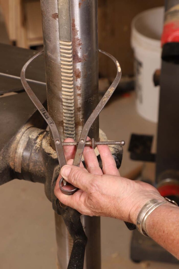 Beth holds a pair of calipers to measure the radius of the drill press post.