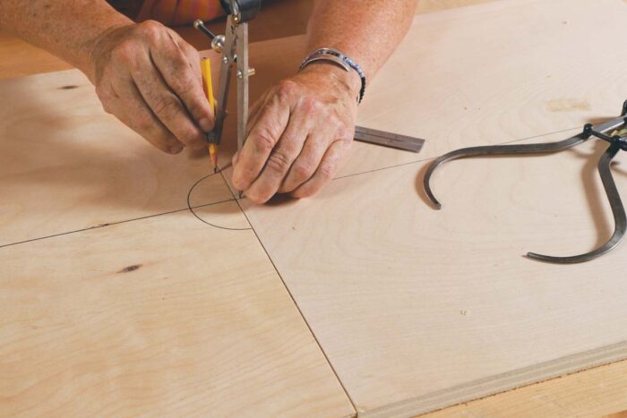 Beth uses a compass to draw a half circle, matching the radius of the drill press post.