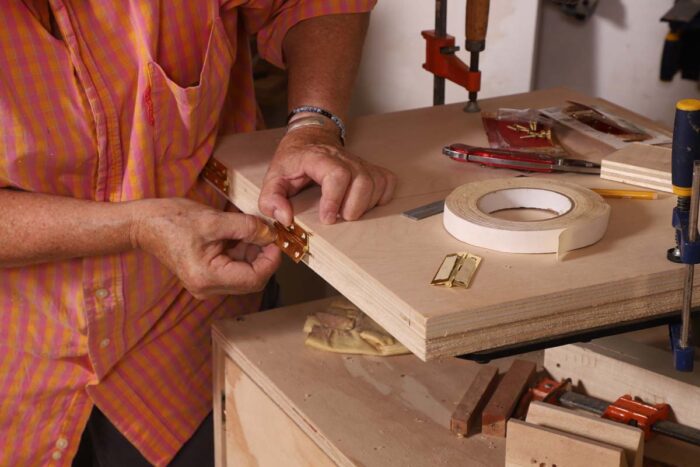 Beth holds a hinge on the edge of two sheets of plywood. 