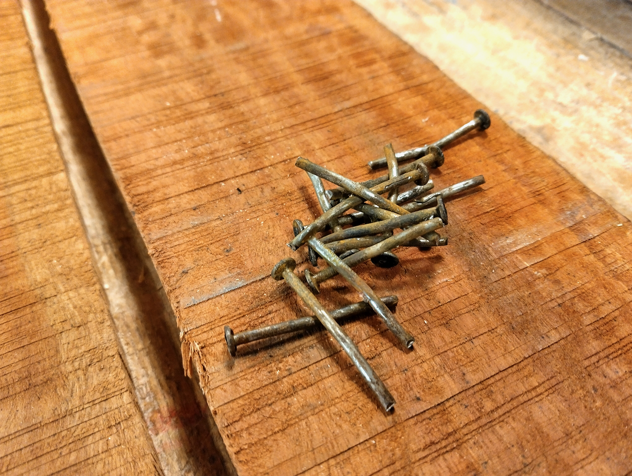 A pile of rusty nails sits on a reclaimed board. 