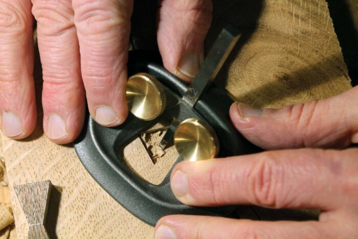 Dave pushes Melbourne tools small router plane in a mortise for a butterfly key. Shavings show he's taking light, controlled passes. 