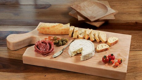 A wooden charcuterie board with slices of cheese and meats on it.