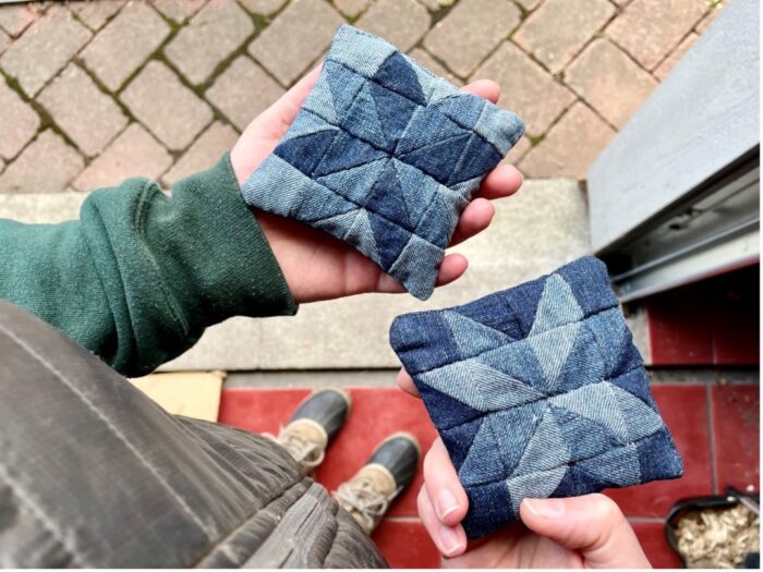 Two hands holding stitched denim pouches filled with rice.